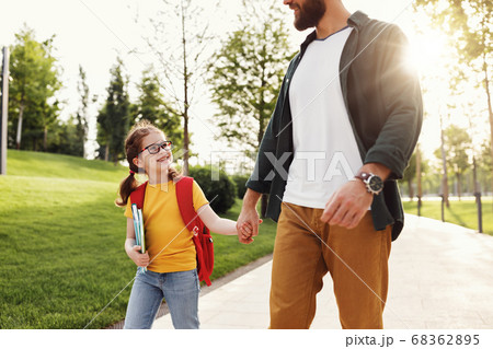 Cheerful schoolgirl walking to school with father Cheerful schoolgirl walking to school with father 68362895