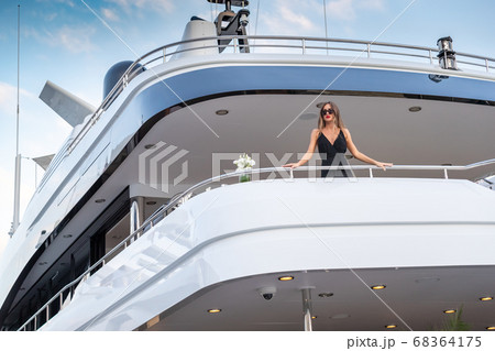 The elegant girl dressed in an evening dress of black color and sunglasses stands on the top deck of a huge yacht in anticipation, red lips, gorgeous lady, she does up hair 68364175