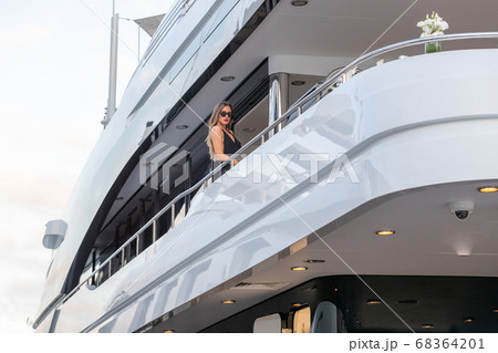 The elegant girl dressed in an evening dress of black color and sunglasses stands on the top deck of a huge yacht in anticipation, red lips, gorgeous lady, she does up hair 68364201