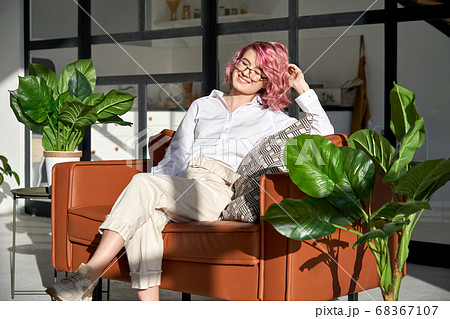 Smiling hipster girl with pink hair relaxing on sofa in sunny cozy living room. 68367107