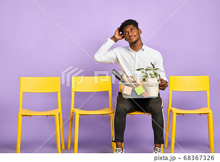 disappointed young dark-skinned man holding box of personal belongings quit job 68367326