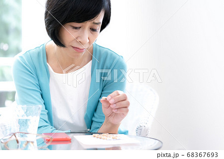 クスリを飲むか悩んでいるミドル女性 68367693