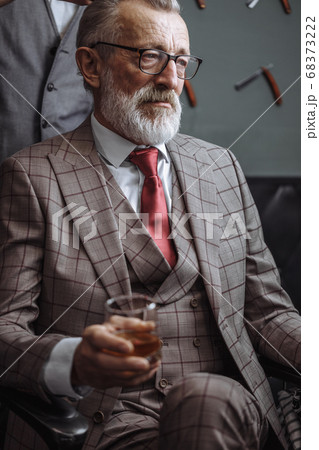 Bearded old businessman sitting at barber shop in chair choosing haircut design Bearded old businessman sitting at barber shop in chair choosing haircut design 68373222