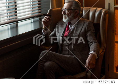 Serene concentrated mature male architector with grey-haired beard smoking cigar 68374183
