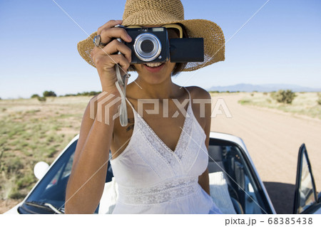 Native American woman in sun dress sitting on white convertible sports car, taking pictures Native American woman in sun dress sitting on white convertible sports car, taking pictures 68385438