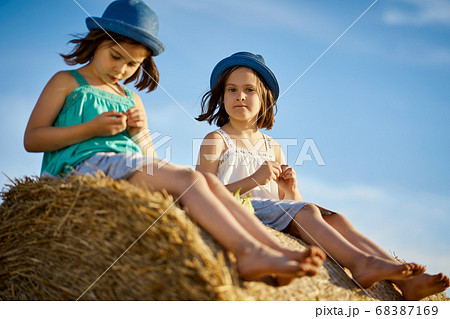 two charming girls are eating sunflower seeds on mown rye in the field two charming girls are eating sunflower seeds on mown rye in the field 68387169