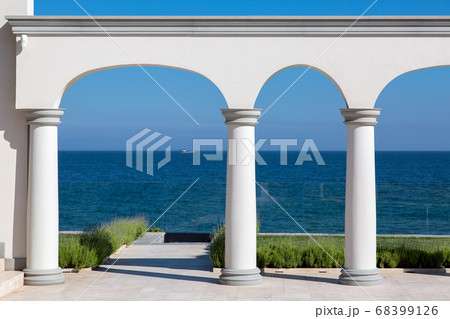 an arch with columns of white stone and a marble floor with a lawn and a view of the sea on the coast of a luxurious mansion. 68399126