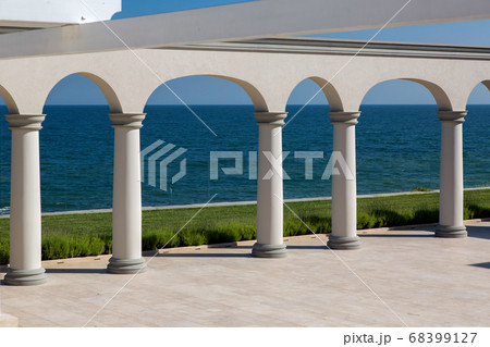 an arch with columns of white stone and a marble floor on sunny day of a luxurious mansion, nobody. an arch with columns of white stone and a marble floor on sunny day of a luxurious mansion, nobody. 68399127