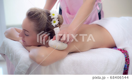 Massage therapist using herbal compress with woman 68406544