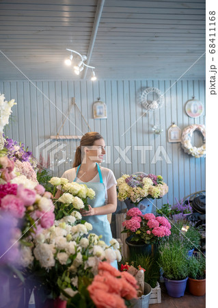 Smiling brown-haired female standing at the flower stand, touching white roses, looking sideways 68411168