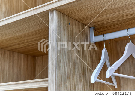 White wardrobe with wooden shelves close-up. Wooden filling of wardrobe and white clothes hangers White wardrobe with wooden shelves close-up. Wooden filling of wardrobe and white clothes hangers 68412173