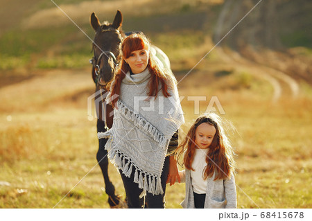 Mother and daughter in a field playing with a horse 68415678