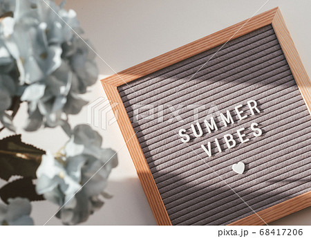 Letter board with words SUMMER VIBES and heart. Top view on flat lay board with quote with symbol of love and romance. Summer sun shining on white background and blue flowers in bloom. 68417206