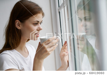woman with a cup of coffee near the window looks at the nature 68419060