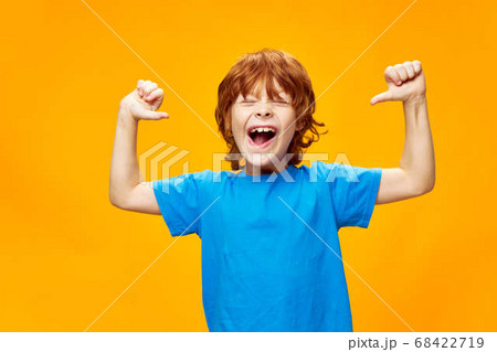 red-haired boy in a blue T-shirt is having fun on a yellow background and pointing at himself 68422719