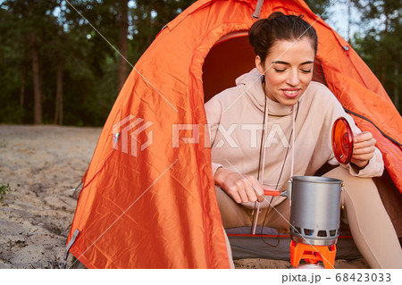 Cheerful female traveler making hot drink during camping Cheerful female traveler making hot drink during camping 68423033