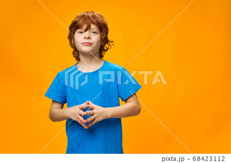 Beautiful red-haired boy in a blue T-shirt joined his fingers  68423112