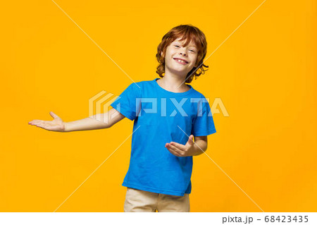 redheaded boy blue t-shirt yellow background freckles and shows with his hands to the side, free space 68423435