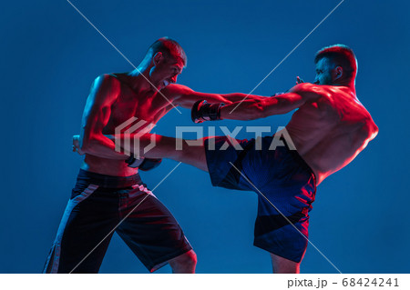 MMA. Two professional fighters punching or boxing isolated on blue studio background in neon MMA. Two professional fighters punching or boxing isolated on blue studio background in neon 68424241