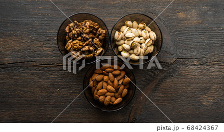 Almond, pistachio and walnut in a small plates which standing on a black table. Nuts is a healthy vegetarian protein and nutritious food. 68424367