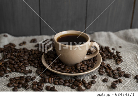 Coffee cup with roasted coffee beans on linen background. Mug of black coffe with scattered coffee beans. Fresh coffee beans. 68424371