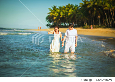 couple in white clothes in water on beach.  68424629