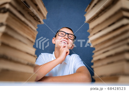 Happy smart boy in glasses sitting between two piles of books and look up smiling Happy smart boy in glasses sitting between two piles of books and look up smiling 68428523