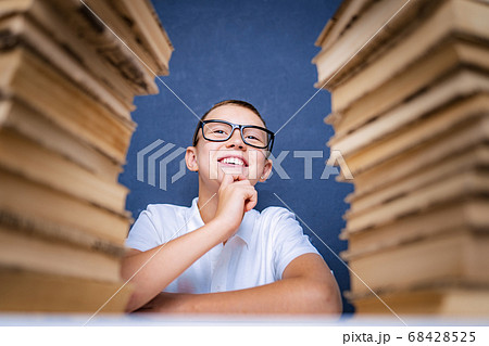 Smart boy in glasses sitting between two piles of books and look up thoughtfully Smart boy in glasses sitting between two piles of books and look up thoughtfully 68428525