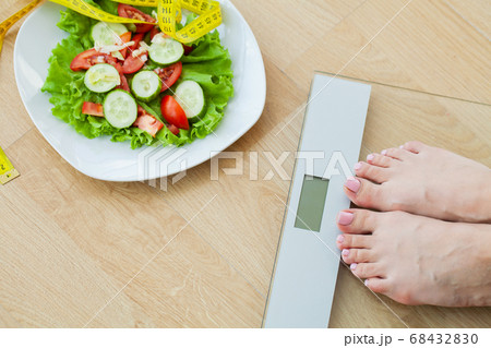Diet concept, woman measures weight on electronic scales and diet salad with yellow measuring tape 68432830