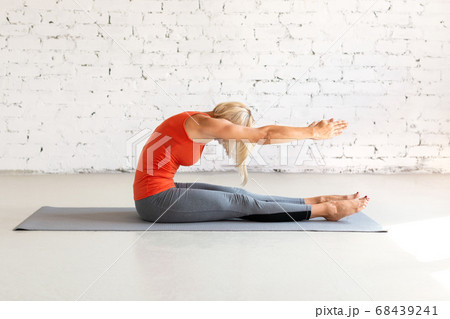 Attractive caucasian woman practice pilates. Seated forward fold on a mat, in loft white studio. Indoor workout, selective focus. 68439241