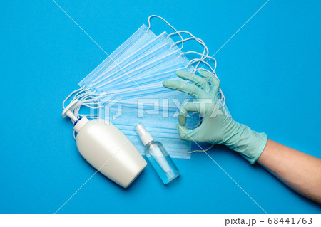 Human hand in protective glove, face protective masks and hand sanitizer or liquid soap isolated over blue background Human hand in protective glove, face protective masks and hand sanitizer or liquid soap isolated over blue background 68441763