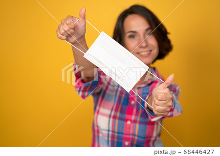 Young woman holding protective mask in foreground with selective focus and copy space on it. Isolated on yellow background. Quarantine concept 68446427