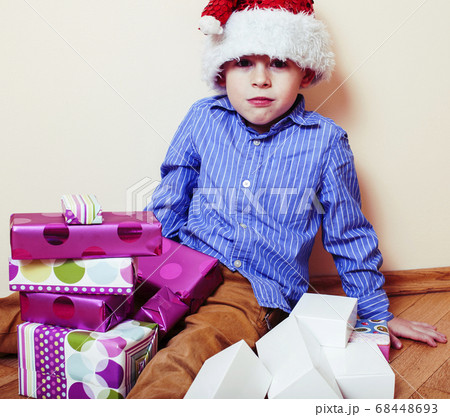 little cute boy with Christmas gifts at home wearing red Santas hat. closeup emotional happy smiling in mess with toys, lifestyle holiday people concept 68448693