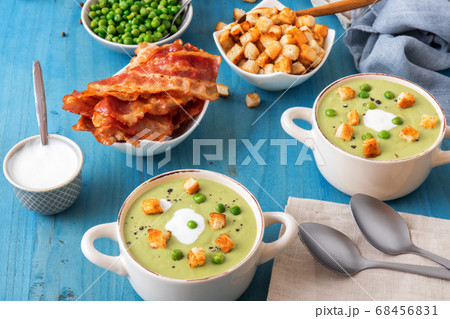 Homemade creamy grean pea soup with slices of grilled bacon and roasted rusks, blue background. Homemade creamy grean pea soup with slices of grilled bacon and roasted rusks, blue background. 68456831