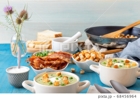 Homemade creamy grean pea soup with slices of grilled bacon and roasted rusks, blue background. Homemade creamy grean pea soup with slices of grilled bacon and roasted rusks, blue background. 68456964
