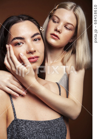 two pretty diverse girls happy posing together: blond and brunette on brown background, lifestyle people concept two pretty diverse girls happy posing together: blond and brunette on brown background, lifestyle people concept 68458610