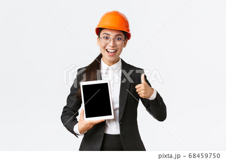 Impressed young female realtor, estate agent showing building during construction, wear safety helmet and business suit, holding digital tablet and make thumbs-up, recommend purchase Impressed young female realtor, estate agent showing building during construction, wear safety helmet and business suit, holding digital tablet and make thumbs-up, recommend purchase 68459750