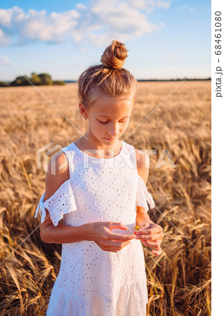 Happy child in wheat field. Beautiful girl in white dress in a straw hat with ripe wheat in hands 68461080