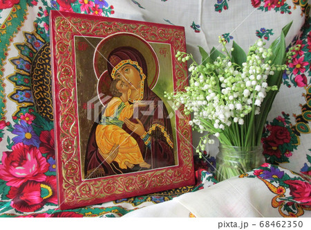 Traditional orthodox icon of the Mother of God. Icon Vladimirskaya. Handwritten icon of the Virgin Mary with Jesus Christ on the background of Ukrainian rushnyks and lilies of the valley. 68462350