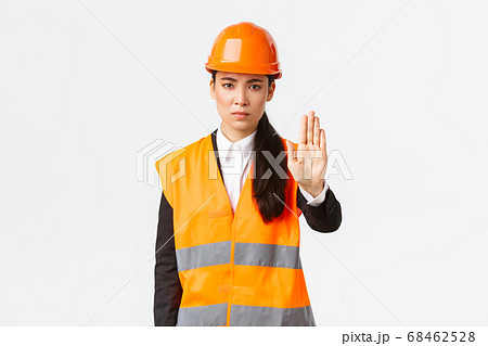 Serious-looking disappointed asian female architect, construction manager at working area wearing safety helmet, showing stop gesture, prohibit action, forbid trespassing, white background Serious-looking disappointed asian female architect, construction manager at working area wearing safety helmet, showing stop gesture, prohibit action, forbid trespassing, white background 68462528