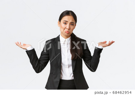 Clueless upset young asian female office worker, manager in black suit, shrugging with hands spread sideways and pouting unaware, dont know, cant understand, standing useless and indecisive 68462954