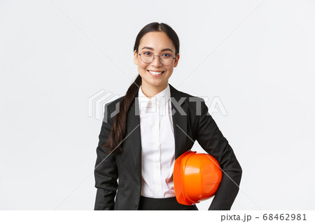 Portrait of happy professiona female asian construction manager, engineer in business suit holding helmet and smiling at camera, entering building area for inspection, white background Portrait of happy professiona female asian construction manager, engineer in business suit holding helmet and smiling at camera, entering building area for inspection, white background 68462981