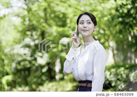 新緑の木々を背にスマホを見ている若い女性 新緑の木々を背にスマホを見ている若い女性 68463099