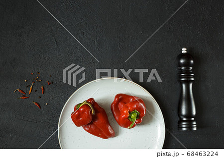 Two shriveled red peppers on a gray plate. Black background with pepper mill and spices Two shriveled red peppers on a gray plate. Black background with pepper mill and spices 68463224
