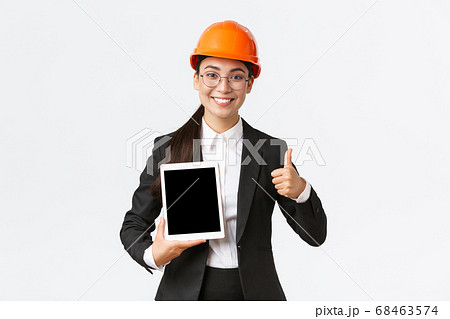 Professional smiling asian female construction manager, factory engineer in business suit and safety helmet showing thumbs-up and digital tablet screen with positive graph, white background Professional smiling asian female construction manager, factory engineer in business suit and safety helmet showing thumbs-up and digital tablet screen with positive graph, white background 68463574