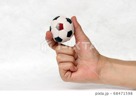 Mini ball of football in hand, hold it with two finger and one black point of football is qatar flag on white background. Mini ball of football in hand, hold it with two finger and one black point of football is qatar flag on white background. 68471598