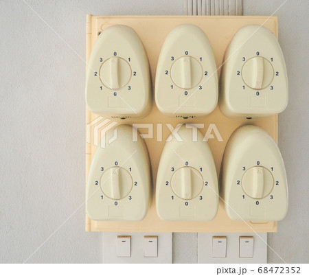 Six white vintage hand-crank fan switches are lined up on a light yellow pedestal underneath, with four light switches on a white concrete wall. Six white vintage hand-crank fan switches are lined up on a light yellow pedestal underneath, with four light switches on a white concrete wall. 68472352
