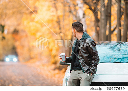 Young man drinking coffee with phone in autumn park outdoors 68477639