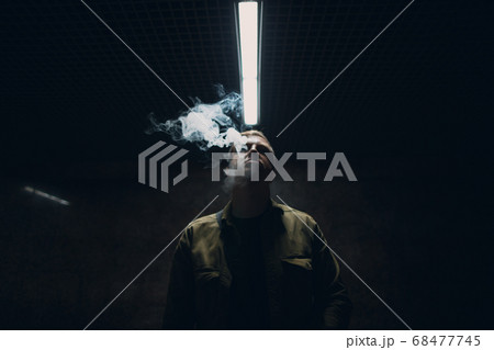 Portrait of young caucasian man smoking e-cigarette in dark with line light 68477745