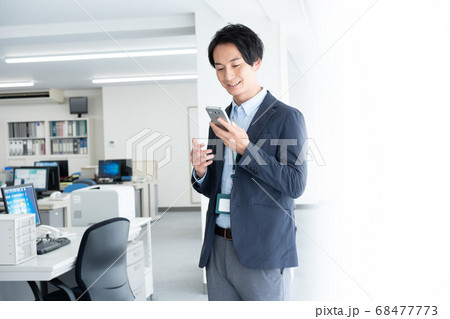 早朝1人でオフィスに出社してスマホで話をする若いビジネスマン 早朝1人でオフィスに出社してスマホで話をする若いビジネスマン 68477773